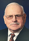 Portrait of an older man in glasses wearing a suit and tie on a dark blue background.