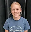 Smiling student in a blue T-shirt posed against a dark curtain.