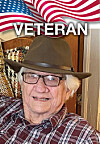 Elderly man in glasses and brown hat seated in front of an American flag graphic with 'VETERAN' text.