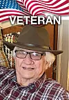 Elderly man in glasses and brown hat seated in front of an American flag graphic with 'VETERAN' text.