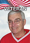 Older man wearing glasses and a red shirt in front of a U.S. flag background with “VETERAN” text.