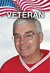 Older man wearing glasses and a red shirt in front of a U.S. flag background with “VETERAN” text.