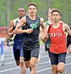 Three runners race on a track during an outdoor meet.