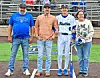 Four people standing on a baseball field near home plate with stadium bleachers behind them.