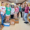 Students standing in a school hallway next to boxes filled with donated food and supplies.