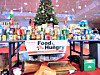 Tables covered with donated food and supplies surround a decorated Christmas tree in a large indoor space.