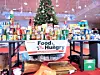 Tables covered with donated food and supplies surround a decorated Christmas tree in a large indoor space.