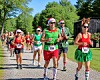 Runners in Santa hats and holiday costumes compete on a paved road surrounded by trees.