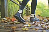 Lower legs of a person walking on a leaf-covered path in autumn.