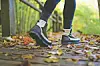 Lower legs of a person walking on a leaf-covered path in autumn.