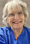 Smiling older woman wearing glasses and a blue jacket in a close-up screenshot.