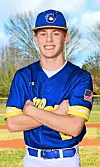 A smiling baseball player in a blue and yellow uniform stands with arms crossed outdoors.