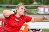 Athlete in a red uniform extending an arm while throwing a discus outdoors.