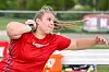 Athlete in a red uniform extending an arm while throwing a discus outdoors.