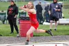 Female athlete in red performs a throwing motion in an outdoor track and field competition.