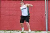 Athlete mid-throw beside a red safety net at an outdoor field event venue.
