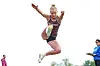 An athlete is captured midair during a jumping event, with officials standing nearby.