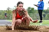 Athlete landing in a sand pit during a long jump, with an official standing nearby.