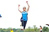Runner in blue raises arms while crossing a track finish line.