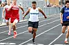 Athletes sprint down an outdoor track, with one runner in front and others close behind.