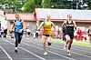 Three runners race on a track with stadium seating behind them.