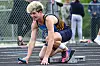 Athlete crouched at the starting line on a track, holding a baton.