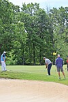 Three golfers on a golf course near a sand trap and green with trees in the background.