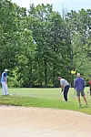 Three golfers on a golf course near a sand trap and green with trees in the background.