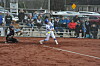 Softball batter swings while catcher crouches and spectators sit behind the backstop.