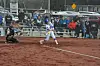 Softball batter swings while catcher crouches and spectators sit behind the backstop.