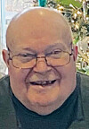Smiling older man wearing glasses in front of a decorated background.