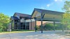 Low-rise brick and glass building with a covered entrance and landscaped surroundings on a sunny day.