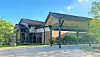 Low-rise brick and glass building with a covered entrance and landscaped surroundings on a sunny day.