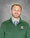 Man in a green pullover with a white H logo poses against a gray background.