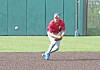 Baseball player in red jersey crouches to field a ground ball on a field.