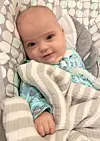 Baby wrapped in a striped blanket resting in a patterned infant seat.