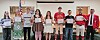 A group of students stand indoors holding certificates during a recognition event.