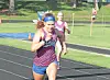 Runner in blue and red uniform leading on an outdoor track with competitors behind.