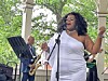 Singer performs at a microphone on an outdoor stage while a saxophonist stands behind her.