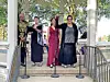 Four performers stand on an outdoor pavilion stage with microphones and music stands.
