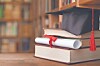 Graduation cap on stacked books beside a blurred bookshelf.