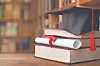 Graduation cap on stacked books beside a blurred bookshelf.