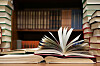 Open books stacked on a table in front of library bookshelves.