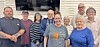 A group of adults poses indoors in two rows, standing close together and facing the camera.