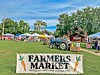 Farmers market booths and a tractor in a park with a Farmers Market sign.