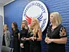 Several women stand indoors beside a Jefferson County School sign mounted on a blue brick wall.