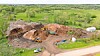 Excavators and other equipment work in a dirt excavation pit beside a road and green countryside.