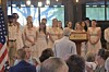 People stand behind a podium during an indoor ceremony as an audience watches.
