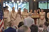 People stand behind a podium during an indoor ceremony as an audience watches.