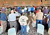 Crowd standing in a banquet hall facing the front of the room during an indoor gathering.
